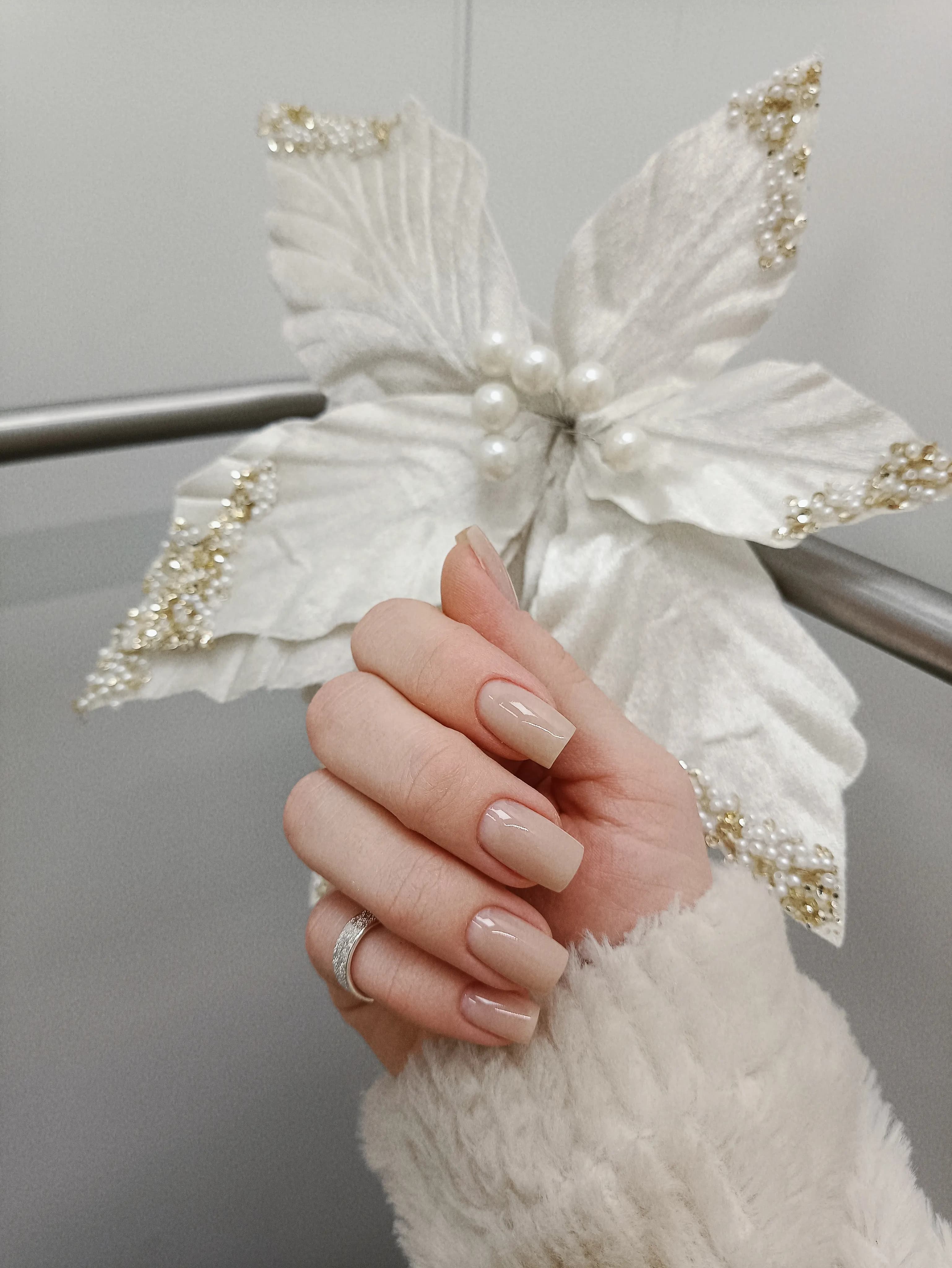 Mão com unhas feitas segurando uma flor branca