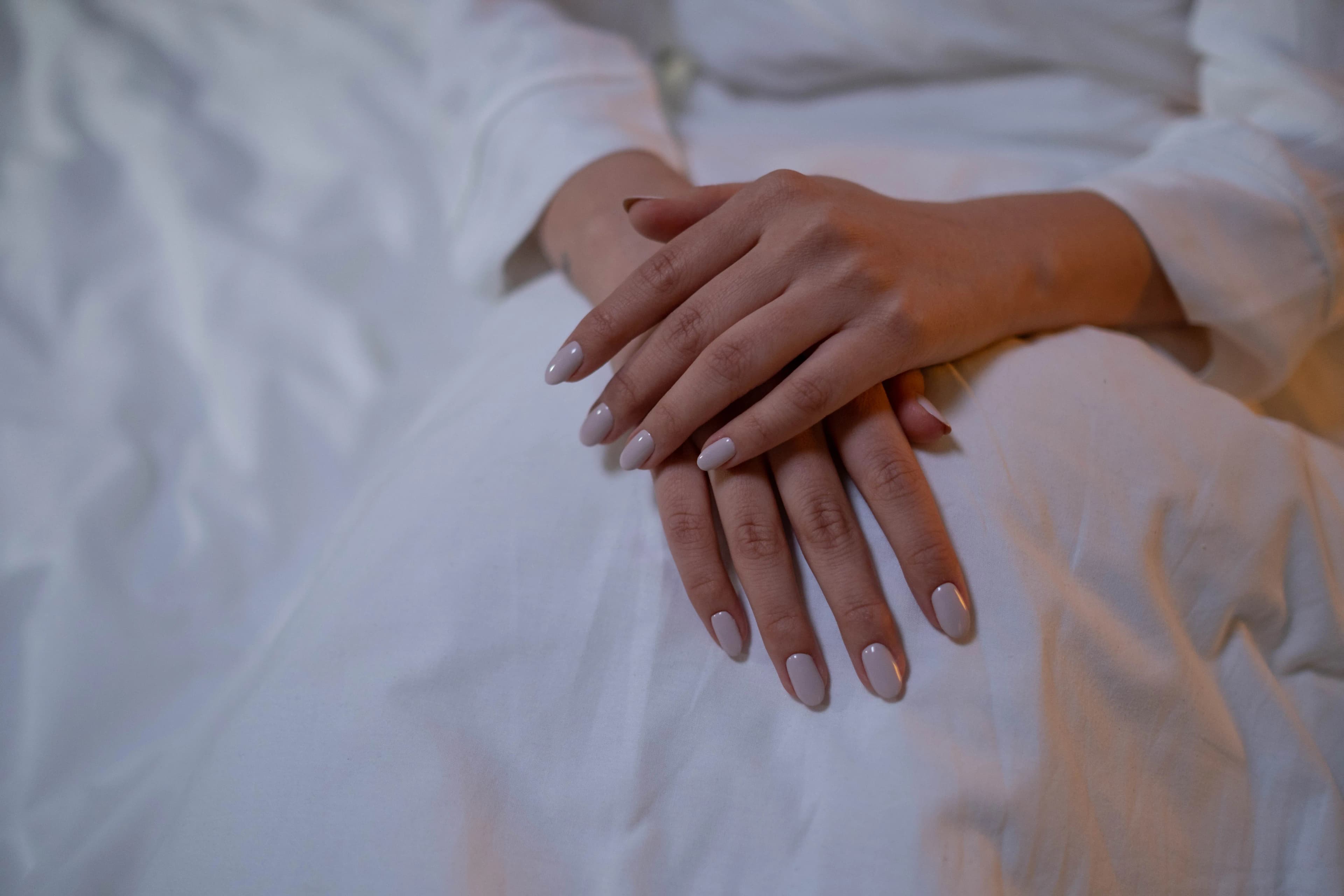 Mãos com unhas nude sobre tecido branco